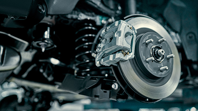 The image shows a close-up view of an automobile s wheel assembly with visible suspension components and the brake disc, set against a blurred background that suggests a workshop environment.