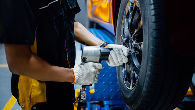 The image shows a person working on the wheel of a vehicle, likely in a professional setting such as a garage or workshop.