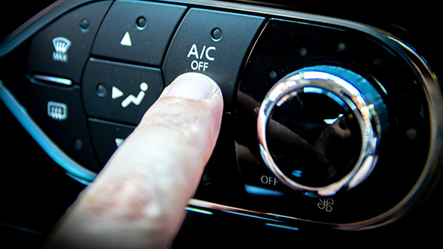 An image of a hand pressing the A C button on a car s dashboard, with the interior lighting illuminating the control panel.